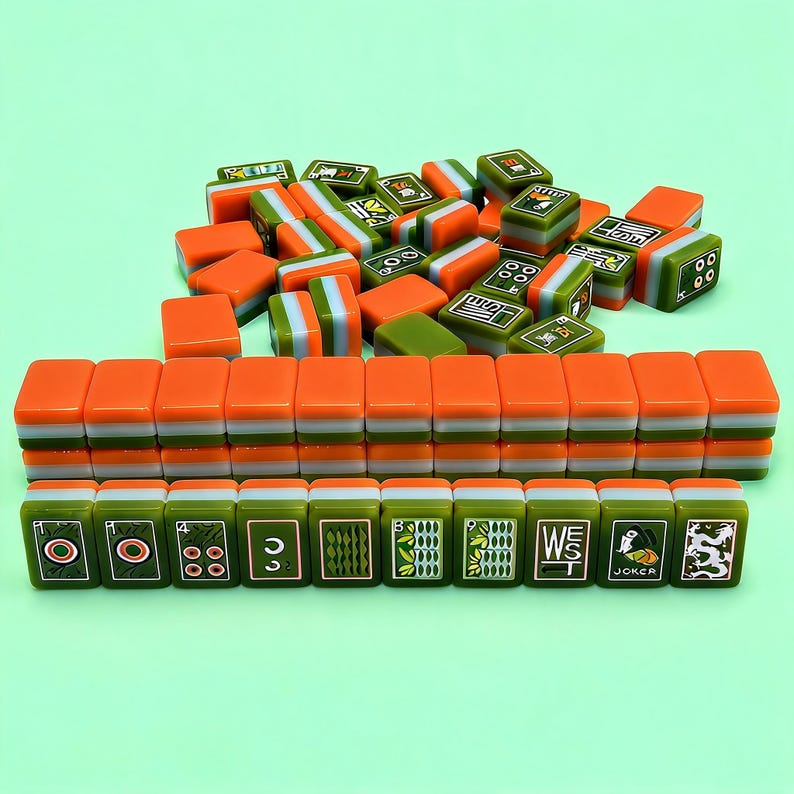 May include: A collection of rectangular mahjong tiles featuring a tri-color design of orange, white, and olive green. Some tiles are arranged in neat rows, while others are scattered in a pile. The front-facing tiles display various symbols.