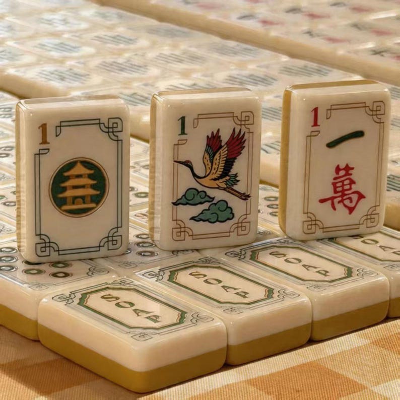 May include: A collection of off-white mahjong tiles with a tan base. Three upright tiles feature a pagoda, a crane, and the number one with a red Chinese character. Other tiles lying flat are labeled with the word SOAP in black capital letters.