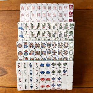 May include: A set of white Mahjong tiles arranged in rows. The tiles feature various designs including Chinese characters, bamboo stalks, circular patterns, the word NEWS with directional arrows, lotus flowers, and Joker labels in red, blue, and green.