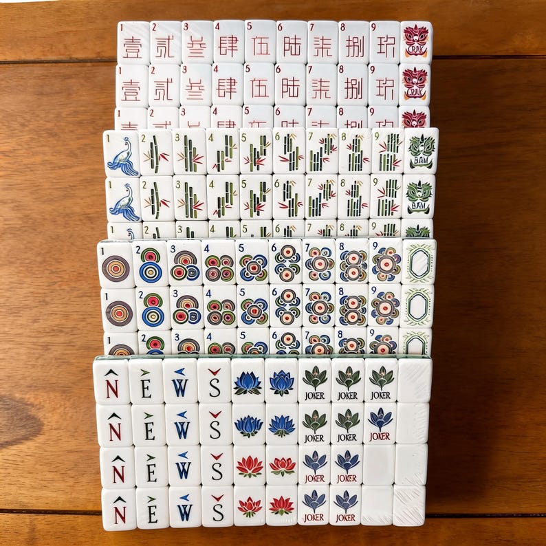 May include: A set of white Mahjong tiles arranged in rows. The tiles feature various designs including Chinese characters, bamboo stalks, circular patterns, the word NEWS with directional arrows, lotus flowers, and Joker labels in red, blue, and green.