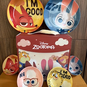 May include: A Disney Zootopia themed dinnerware set featuring two large plates and four small bowls. The plates and bowls display colourful character illustrations of Nick Wilde, Judy Hopps, Clawhauser, and Bellwether with text including I'M GOOD and Hi.