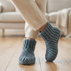 Puede incluir: Un par de zapatillas de estar por casa color azul pizarra que llegan hasta el tobillo, confeccionadas con hilo de punto grueso. Las zapatillas presentan un puño acanalado en la parte superior y un patrón de espiga texturizado en el pie.
