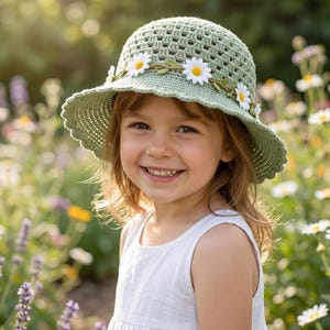 Peut inclure: Un chapeau bob en crochet vert sauge avec un bord festonné et une bande décorative de fleurs marguerites blanches aux centres jaunes. Le chapeau présente un motif ajouré autour de la calotte et une texture en crochet solide sur le bord.