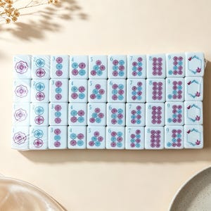 May include: A set of white rectangular mahjong tiles arranged in a grid, featuring blue and purple floral patterns and numbers one through nine. Each tile displays a distinct arrangement of circular flower motifs, with some tiles showing a hexagonal frame.