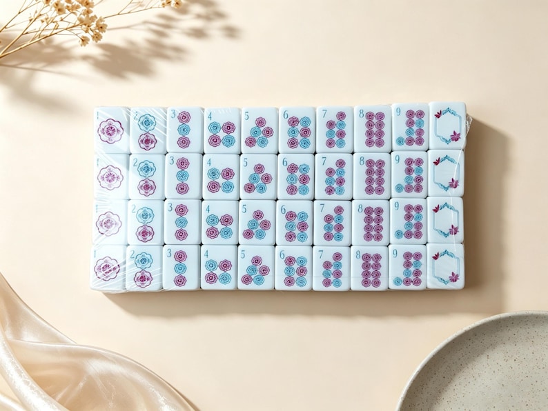 May include: A set of white rectangular mahjong tiles arranged in a grid, featuring blue and purple floral patterns and numbers one through nine. Each tile displays a distinct arrangement of circular flower motifs, with some tiles showing a hexagonal frame.