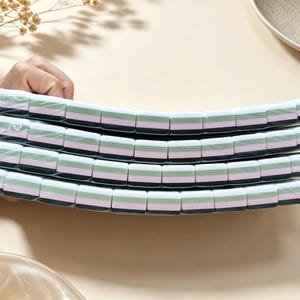 May include: Four rectangular erasers stacked vertically, each featuring a layered design with horizontal stripes of white, light green, pink, and dark gray. The erasers are individually wrapped in clear plastic film and have rounded edges.