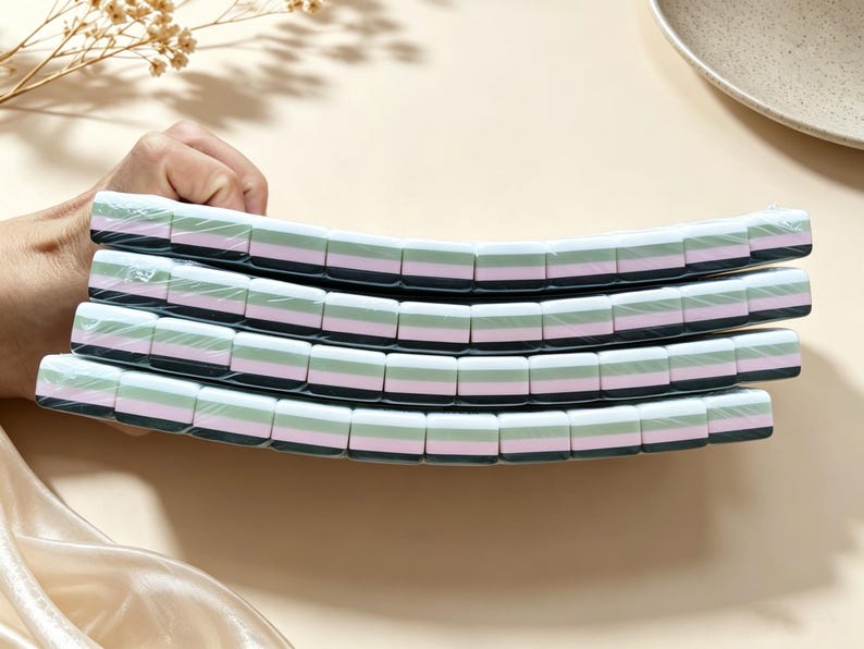 May include: Four rectangular erasers stacked vertically, each featuring a layered design with horizontal stripes of white, light green, pink, and dark gray. The erasers are individually wrapped in clear plastic film and have rounded edges.