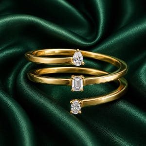 Peut inclure: Une bague en or au design en spirale avec trois pierres transparentes distinctes. Les pierres sont taillées en différentes formes, notamment une taille poire, une taille émeraude et une taille ovale, placées aux extrémités et au centre de l'anneau.