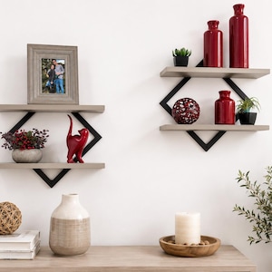 May include: Two wall-mounted shelves featuring light wood planks and black metal diamond-shaped frames. The shelves hold a gray picture frame, a red cat figurine, a potted plant, three red vases, and a decorative red sphere with white accents.