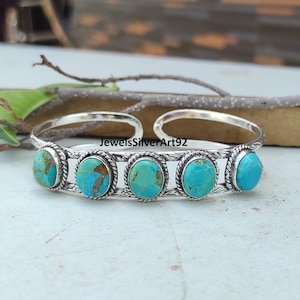 May include: A silver cuff bracelet featuring five oval turquoise stones set in twisted rope borders. The metal band has an engraved leaf pattern along the sides. The text JewelsSilverArt92 is visible in the centre of the open cuff design.