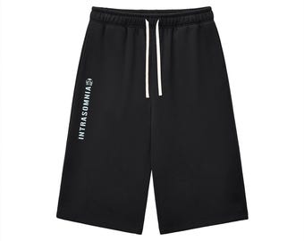 Puede incluir: Pantalones cortos negros con cintura elástica y cordones blancos. La pierna derecha muestra el texto blanco INTRASOMNIA orientado verticalmente, acompañado de un pequeño icono gráfico blanco situado sobre las letras.