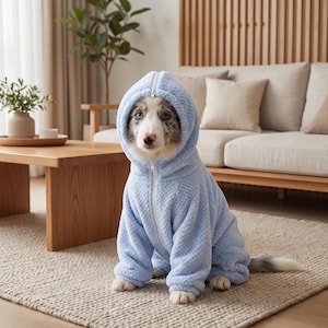 Pode incluir: Um moletom com capuz para animal de estimação em fleece azul claro texturizado com fecho de zíper frontal. A peça apresenta um padrão de diamante acolchoado no tecido e um capuz que emoldura o rosto de um cão com pelo branco e cinza.