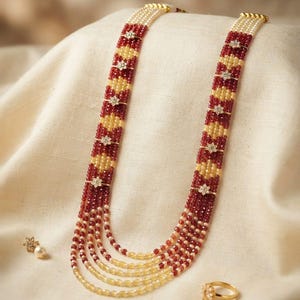 May include: A multi-strand necklace featuring alternating rows of deep red and pale yellow faceted beads, accented with small gold-toned flower-shaped spacers. The set includes a matching single flower stud earring and a gold-toned ring with a flower motif.