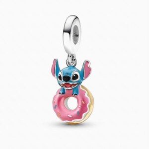 May include: A silver charm featuring a blue character with large ears and a wide smile, holding onto a pink donut with colorful sprinkles. The charm has a polished silver bail at the top for attachment to a bracelet or necklace chain.