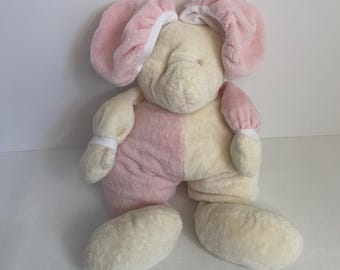 May include: A plush elephant toy featuring a soft, cream-colored head and body with large, floppy pink ears. The stuffed animal has a two-toned design with alternating cream and pink sections on its limbs and torso, and small pink eyes.