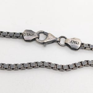 May include: A dark silver-toned box chain necklace featuring a lobster claw clasp. The metal components are oxidized, giving the chain a weathered appearance. The clasp and the adjacent metal tag are both clearly stamped with the word ITALY.