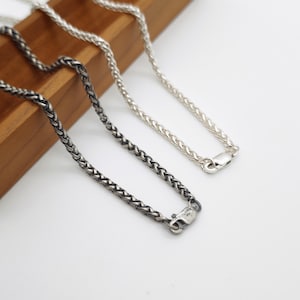 May include: Two wheat chain necklaces, one in a bright polished silver finish and one in a darkened oxidised silver finish. Each chain features a woven link design and a secure lobster claw clasp closure at the end of the metal chain strands.