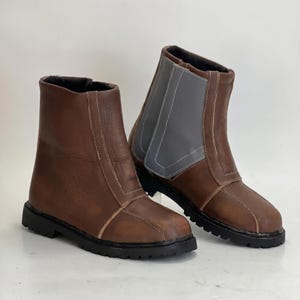 K&ouml;nnte beinhalten: Ein Paar braune Stiefeletten mit glatter Oberfl&auml;che, hellen N&auml;hten und einer dicken schwarzen Profilsohle. Ein Stiefel zeigt ein markantes graues Seitenteil mit Ziern&auml;hten, beide verf&uuml;gen &uuml;ber einen hoch geschnittenen Schaft.