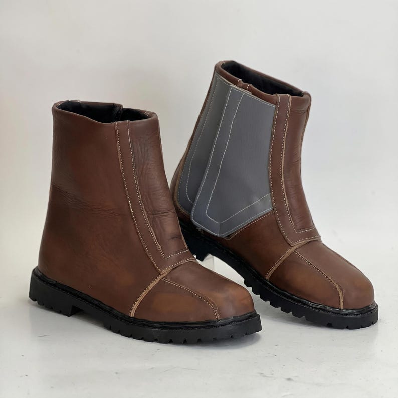 K&ouml;nnte beinhalten: Ein Paar braune Stiefeletten mit glatter Oberfl&auml;che, hellen N&auml;hten und einer dicken schwarzen Profilsohle. Ein Stiefel zeigt ein markantes graues Seitenteil mit Ziern&auml;hten, beide verf&uuml;gen &uuml;ber einen hoch geschnittenen Schaft.