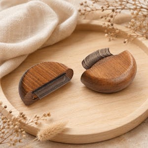 May include: Two semi-circular wooden grooming tools with fine metal teeth. Each tool features a smooth, polished brown wood handle shaped like a half-circle, with a row of thin, closely spaced metal tines extending from the flat edge of the wood.