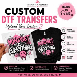Könnte beinhalten: Ein individueller DTF-Transferbogen und ein schwarzes T-Shirt mit einem Grafikdesign, das den Text Mindset Is Everything in Pink und Weiß zeigt, ergänzt durch pinke Farbspritzer, schwarze Tintentropfen und ein pinkes Smiley-Gesicht.