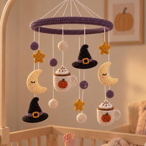 May include: A crochet baby mobile featuring a purple ring suspended by white strings. Hanging elements include two black witch hats with yellow bands, two yellow crescent moons, two white mugs with pumpkin designs, and several small purple and white spheres.