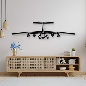 Puede incluir: Una pieza de arte mural de metal negro con la forma de la vista frontal de un gran avión de carga. El diseño presenta una configuración de cola en T, alas montadas en la parte superior y cuatro motores a reacción bajo las alas, en silueta.