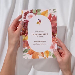 Könnte beinhalten: Eine rechteckige Einladungskarte zum Thanksgiving-Dinner mit einem Aquarell-Blumenrand und Herbstblättern in Rot-, Orange- und Gelbtönen. In der Mitte befindet sich ein weißer ovaler Rahmen mit dem Text: YOU'RE INVITED TO THANKSGIVING DINNER 2026 NOVEMBER 26 7:00 PM - 10:00 PM 123 ANYWHERE ST., ANY CITY.