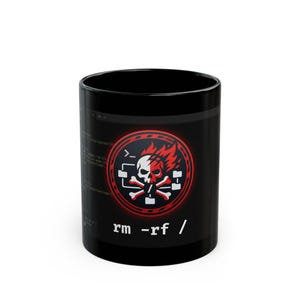 May include: A black ceramic mug featuring a graphic of a skull with flames and crossed bones inside a red circular emblem. Below the emblem, the white text reads rm -rf /. The design includes a faint background of computer code lines.