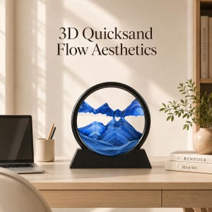 May include: A circular 3D quicksand art piece with a black frame and base, featuring layered blue and white sand forming mountain-like shapes. The text 3D Quicksand Flow Aesthetics is displayed above the object, which sits on a wooden desk.