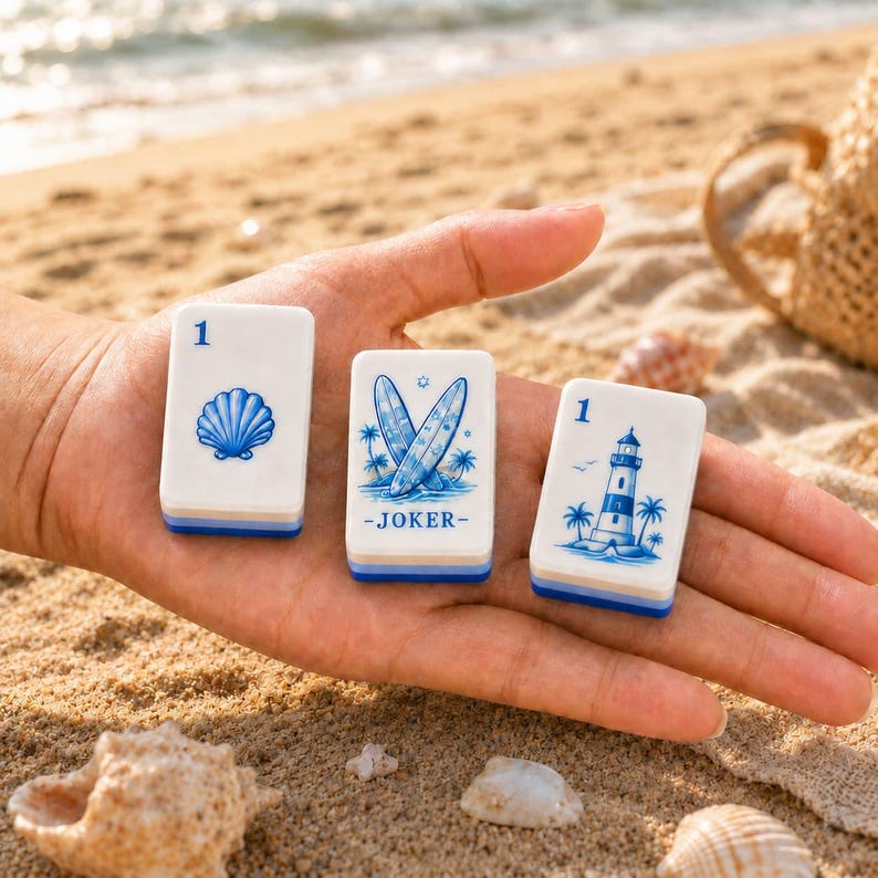 May include: Three rectangular white tiles with blue illustrations. The left tile shows a seashell and the number 1. The center tile features two surfboards and the text JOKER. The right tile displays a lighthouse, palm trees, and the number 1.