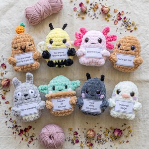 Puede incluir: Una colección de ocho pequeños peluches de ganchillo de diversas formas y colores, incluyendo una abeja, un ajolote y otras criaturas. Cada peluche sostiene una pequeña tarjeta blanca con texto impreso en inglés o sueco, como 'You are enough' y 'Du sprider glädje'.
