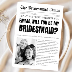 May include: A white rectangular card designed as a newspaper titled The Bridesmaid Times. It features the headline EMMA, WILL YOU BE MY BRIDESMAID?, a black and white photograph of two people, and a printed letter asking a friend to be a bridesmaid.