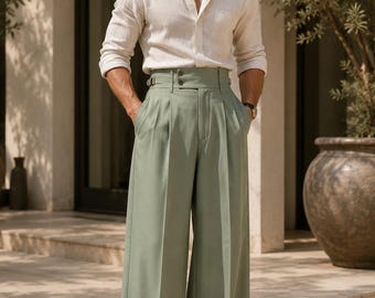 May include: A beige long-sleeved button-down shirt paired with high-waisted, wide-leg sage green trousers featuring a double-button closure, side adjusters, and a pleated front. The outfit is completed with light-colored loafers and dark sunglasses.
