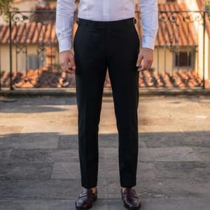 May include: A pair of black trousers featuring a high-waisted design with side adjusters at the waistband, paired with a crisp white long-sleeved button-down shirt and dark brown leather loafers, creating a clean and structured appearance.