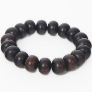 May include: A circular stretch bracelet composed of numerous smooth, round beads in varying shades of dark brown and black. The beads have a matte finish and are strung together in a continuous loop, creating a simple, uniform design for the wrist.
