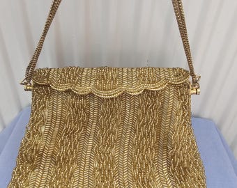 May include: A gold beaded handbag featuring a scalloped flap closure and a matching gold chain strap. The exterior is covered in intricate, vertical rows of metallic gold seed beads arranged in a chevron pattern, creating a textured surface.