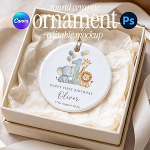 May include: A round white ceramic ornament featuring a watercolor illustration of a blue elephant, a giraffe, and a lion next to a large number one. The text reads HAPPY FIRST BIRTHDAY, Oliver, and 17th August 2026. It hangs by a gold string.