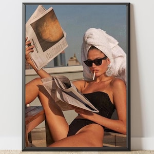 Peut inclure: Une impression d'art mural encadrée montrant une personne en maillot de bain noir sans bretelles, une serviette blanche sur la tête et des lunettes de soleil noires, tenant un journal Science Times. La personne a une cigarette et porte des boucles d'oreilles.