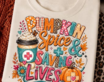 May include: A cream-colored t-shirt featuring a graphic print with the text PUMPKIN SPICE & SAVING LIVES. The design includes a coffee cup with a medical cross, a pumpkin with a bandage, a stethoscope, autumn leaves, and colorful patterns.