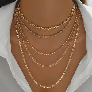 Peut inclure: Un ensemble de cinq colliers superposés de couleur dorée. Le lot comprend une chaîne à maillons ovales épais, une chaîne torsadée, une fine chaîne à perles, une chaîne à maillons rectangulaires allongés et une chaîne à maillons marins plats.