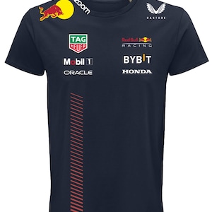 以下が含まれることがあります： 前面にRed Bull、Zoom、Castore、Tag Heuer、Mobil 1、Oracle、Red Bull Racing、Bybit、Hondaのロゴがプリントされ、サイドに赤い細い斜線の垂直パターンがあしらわれた、ダークネイビーの半袖Tシャツ。