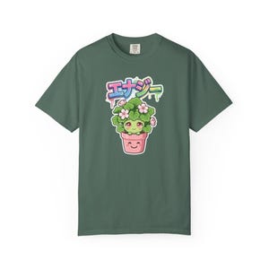 Peut inclure: Un t-shirt vert foncé arborant un motif de plante verte anthropomorphe souriante avec des fleurs roses dans un pot rose. Au-dessus de la plante, le texte japonais エナジー est écrit dans une police arc-en-ciel avec un effet de peinture qui coule.