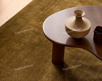 May include: A solid olive green area rug with a short, dense pile texture. A dark brown wooden coffee table with a curved edge sits on the rug, holding a speckled beige ceramic vase and a small dark brown ceramic container.