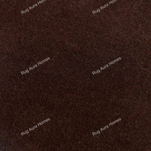 May include: A dark brown rug with a dense, short-pile texture. The surface features a repeating watermark text that reads Rug Aura Homes in a light font, distributed across the fabric to indicate the brand identity of the textile product.