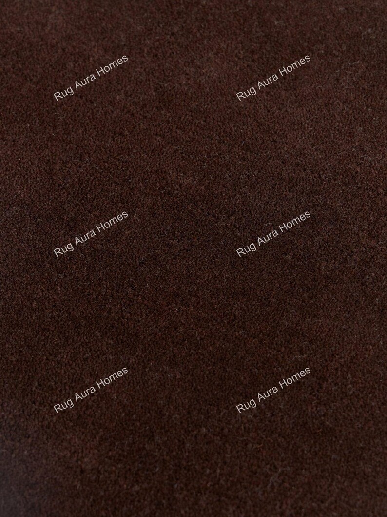 May include: A dark brown rug with a dense, short-pile texture. The surface features a repeating watermark text that reads Rug Aura Homes in a light font, distributed across the fabric to indicate the brand identity of the textile product.
