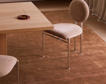 May include: A dining chair with a circular backrest and a square seat, both upholstered in a light beige fabric. The chair features a frame made of four slender, polished chrome metal legs that extend upward to support the backrest and seat.
