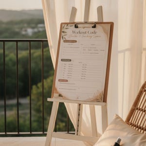 May include: A wooden clipboard with a printed workout planner titled Workout Code Builder & Tracking Space, featuring sections for goals, weekly routines, and notes, displayed on a white wooden easel with a neutral beige botanical design.