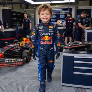 以下が含まれることがあります： Oracle、Red Bull、Bybitなどのスポンサーロゴが入った、ダークブルーとレッドのレーシングスーツを着た子供。スーツにはハイカラー、長袖、お揃いのダークブルーのグローブが備わっており、プロ仕様のレーシングギアを模したデザインになっています。