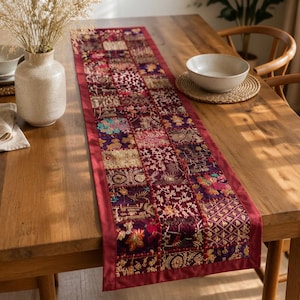 May include: A rectangular table runner featuring a patchwork design of various fabric squares in shades of deep red, purple, gold, and orange. The runner has a solid red border and displays intricate embroidered patterns and floral motifs.